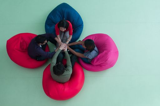 Four people sitting in coloured bean bags holding hands