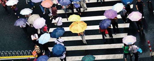 KPMG IFRS Insurance topic image: crowd crossing a street carrying open umbrellas