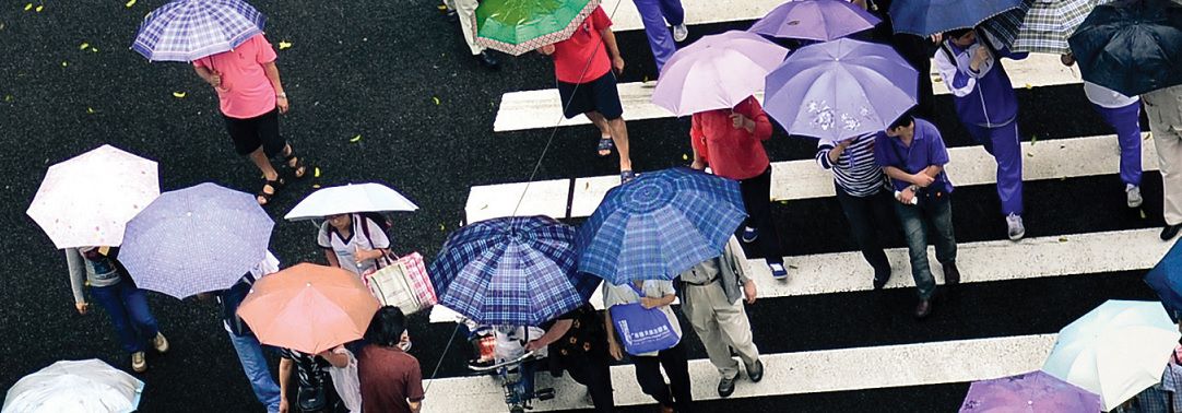 KPMG IFRS Insurance topic image: crowd crossing a street carrying open umbrellas