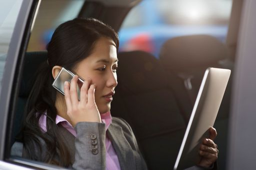 Businesswoman using phone and tablet in car