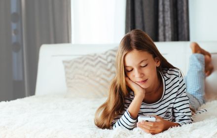A girl resting on bed while looking at phone