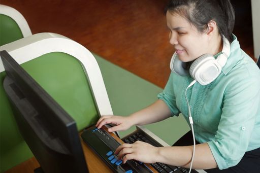 Blind person wearing headphones using computer with braille