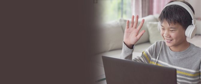 Boy sitting in front of laptop wearing headphones and waving hand banner