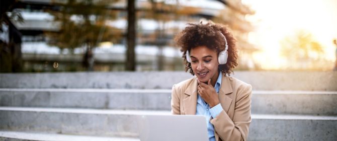 Business woman on a lunch break outdoors using laptop with headphones