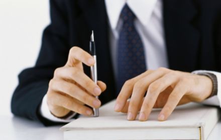 Businessman's hands on a book whilst holding a pen