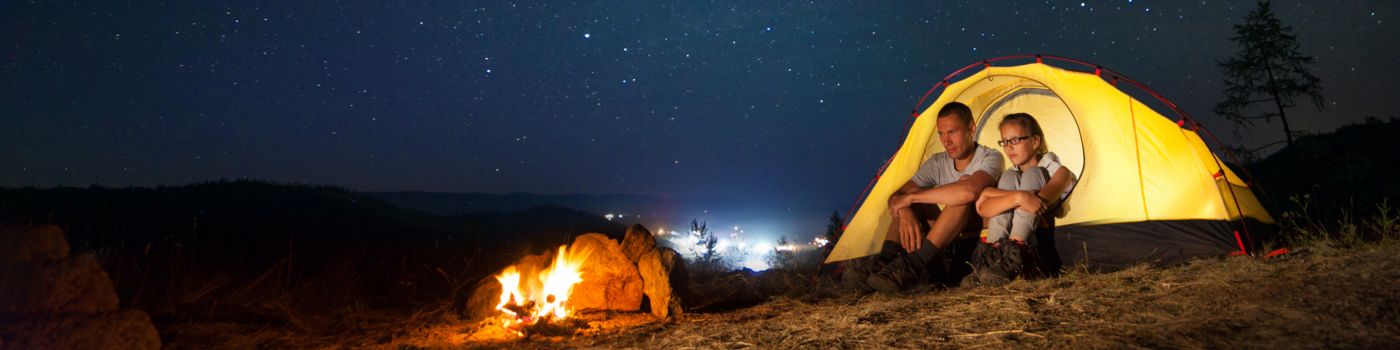 People camping in a yellow tent beneath the stars