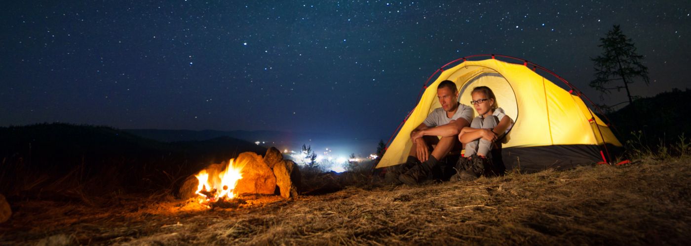 People camping in a yellow tent under a starry sky