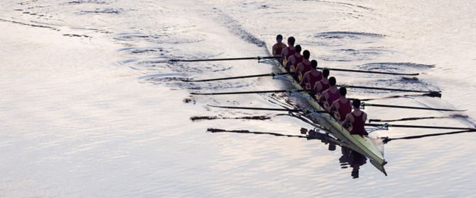 A rowing team practices on a calm lake