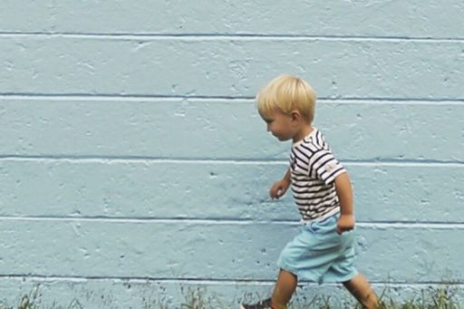 Little boy walking on grass in front of blue wall