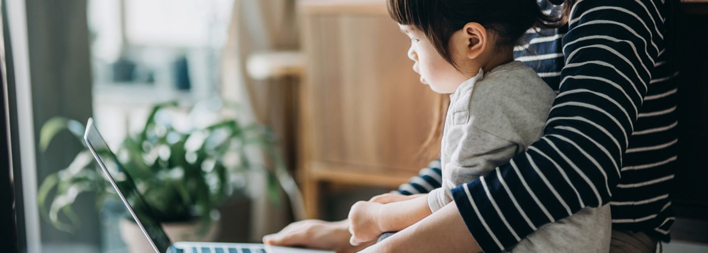 Mother using laptop and working from home while taking care of little daughter