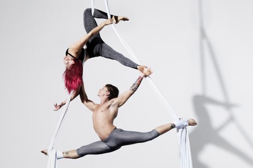 Circus artists in silks with shadows projected on white wall