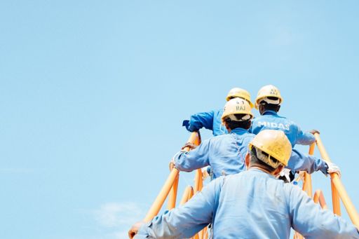 Back view of construction workers wearing yellow helmets climbing up the stairs