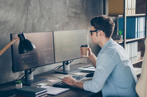Employee testing computer while sitting at a desk holding a take-out mug in workplace