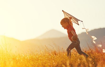 Happy child girl with a kite running on meadow in summer