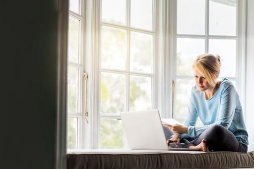 Woman sits on a window sill with her laptop