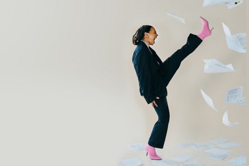 Frau im Anzug streckt Bein nach oben und Papiere fliegen