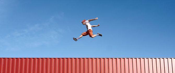 freerunner jumping on red container in front of blue sky