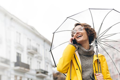 Girl holding an umbrella and wearing a yellow jacket is laughing while talking on the phone