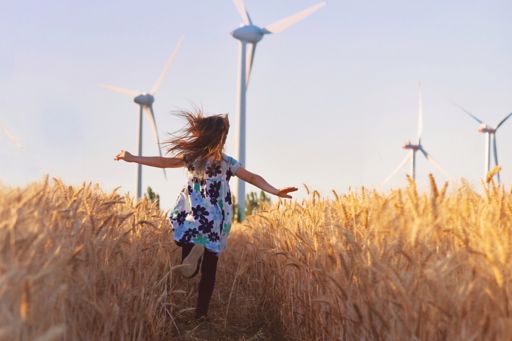 Girl running through field with wind turbines
