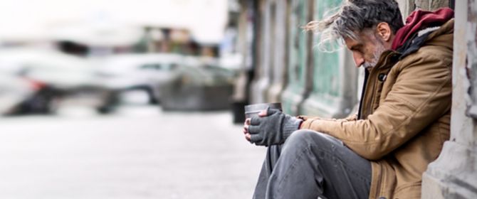 Homeless beggar man sitting outdoors in city asking for money donation.