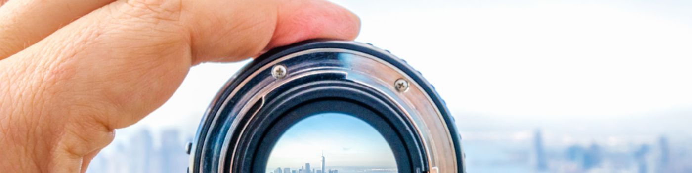 Human hand holding camera lens capturing city view