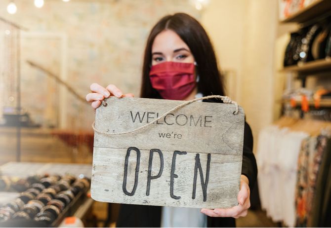 Retail worker wearing mask and holding Open sign