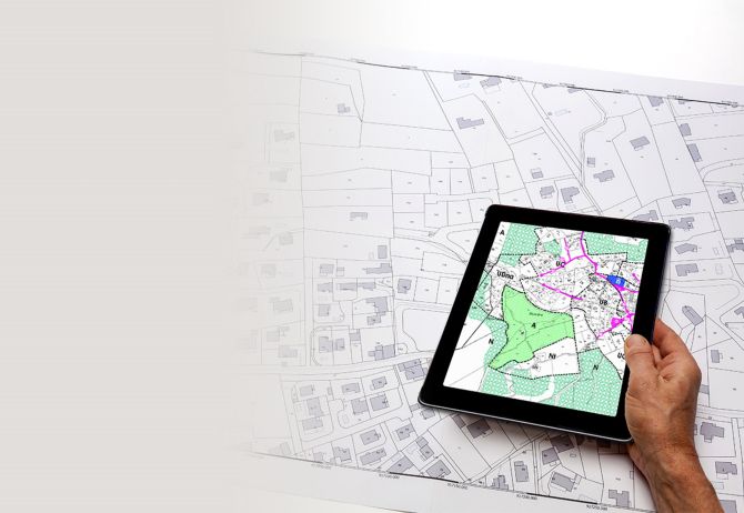 Town planning and land use planning - hand holding a digital tablet displaying a local urban plan, above a cadastral plan placed on a desk