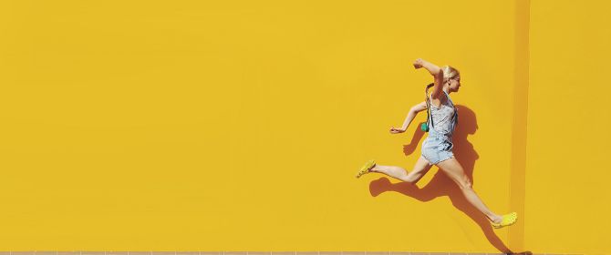 Woman jumps infront of yellow wall