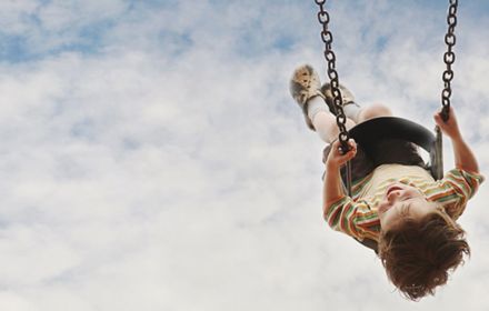 Little boy in striped t-shirt swinging on a swing with clouds and sky in background