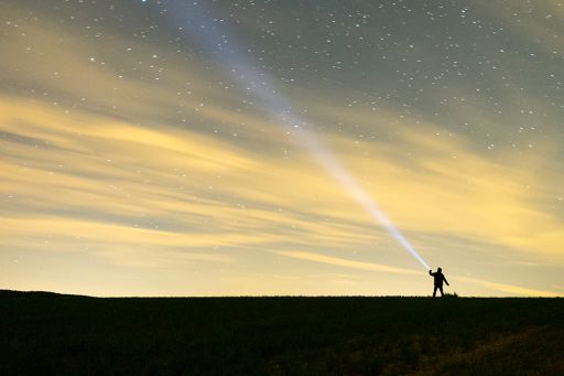 Man flashing light towards the sky full of stars
