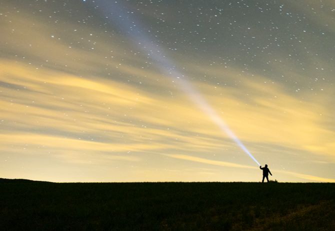 Man flashing light towards the sky full of stars