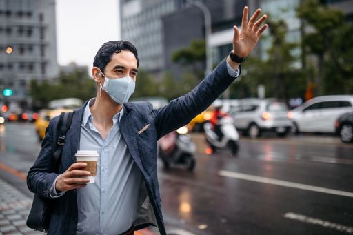 Man in mask waiving hand at taxi holding coffee