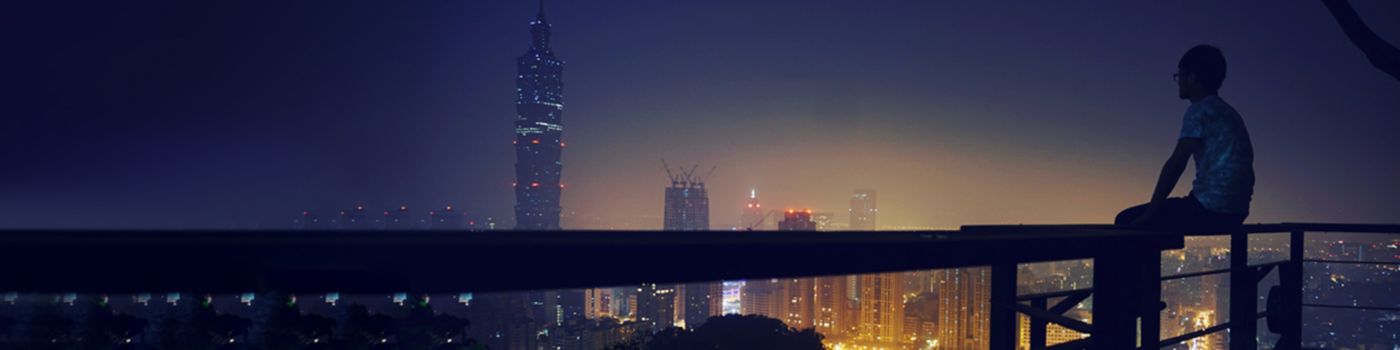 Man sitting on balcony railing and looking at city view