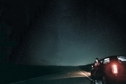 Man standing against car under a starlit sky looking at his phone