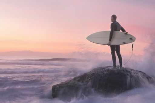 Man standing on a cliff with a surfboard