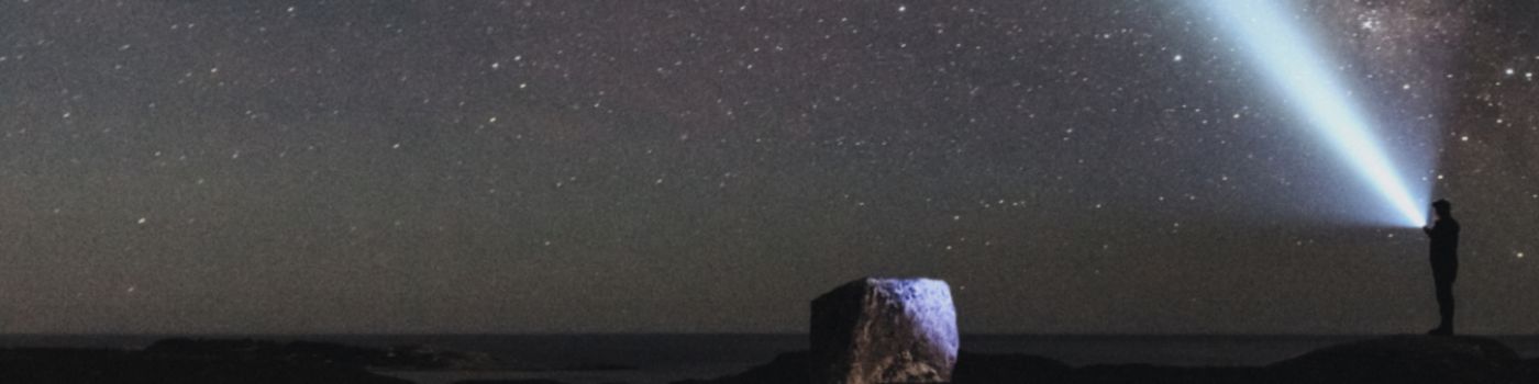 Person mit Taschenlampe strahlt sternübersäten Nachthimmel an