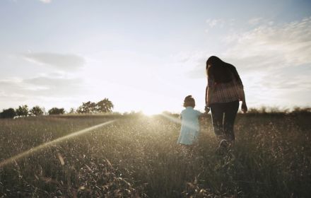 Mom and child walking through a wheat field at sunrise