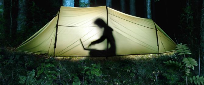 Person inside tent working on laptop in forest at night