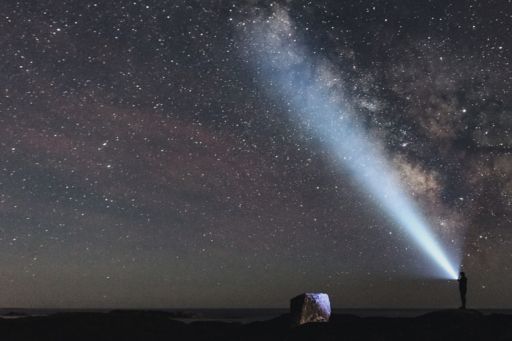Person mit Taschenlampe strahlt sternübersäten Nachthimmel an