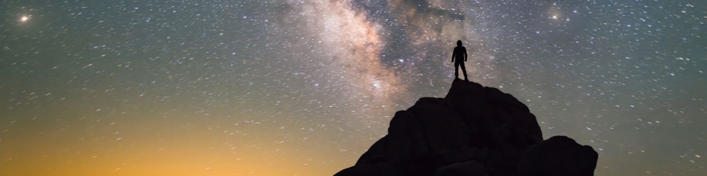 Person standing on a mountain looking at the milky way