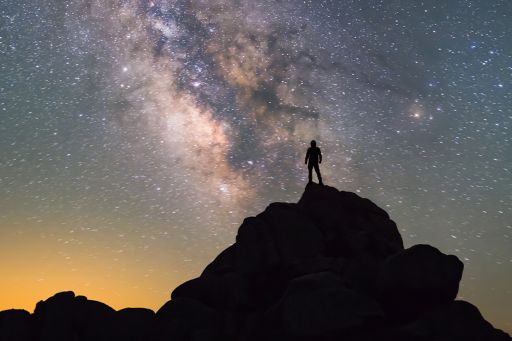 Person standing on a mountain looking at the milky way