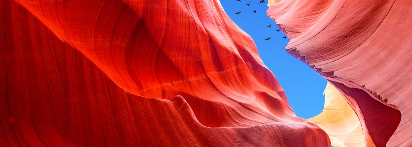 Red mountains beneath blue sky with flying birds