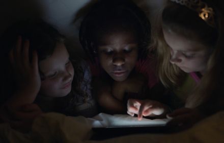 Three kids using a tablet in bed