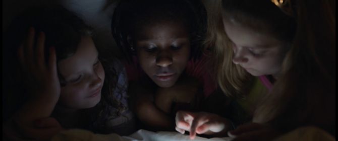 crianças deitadas na cama de bruços olhando para um tablet