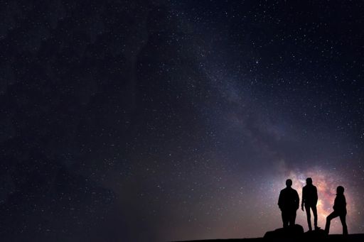 Three people standing under start in night sky