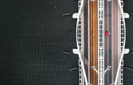 Top view of a giant white bridge over sea with red car