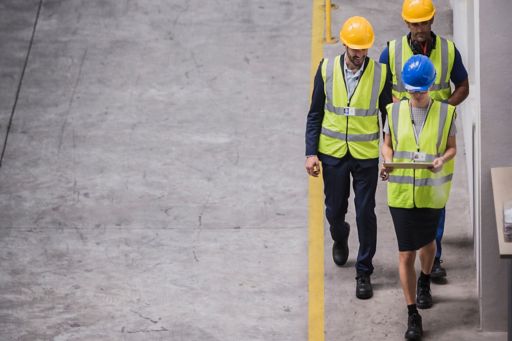 Two men one woman wearing helmet and safety jacket walking looking into tab