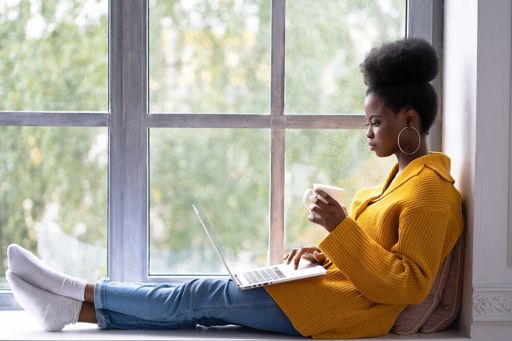 Woman at window with coffee and laptop