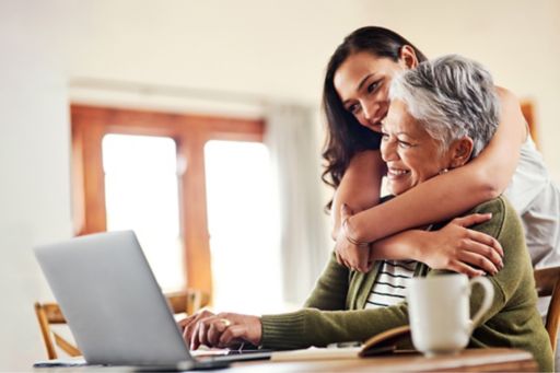 Young woman hugging her grandmother before helping her with her finances on a laptop