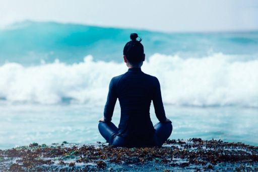 Woman in black wetsuit meditating on beach